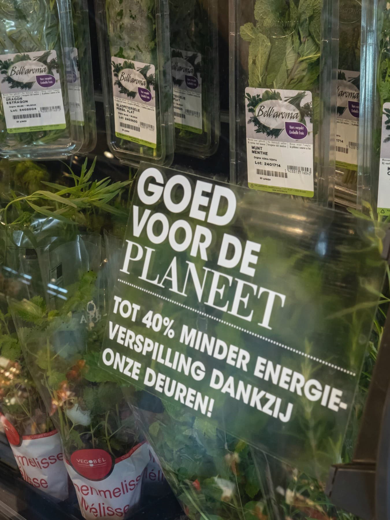 Kruidenrek in de supermarkt met op de glazen deur de tekst: "goed voor de planeet, tot 40% minder energieverspilling dankzij deze deuren!"