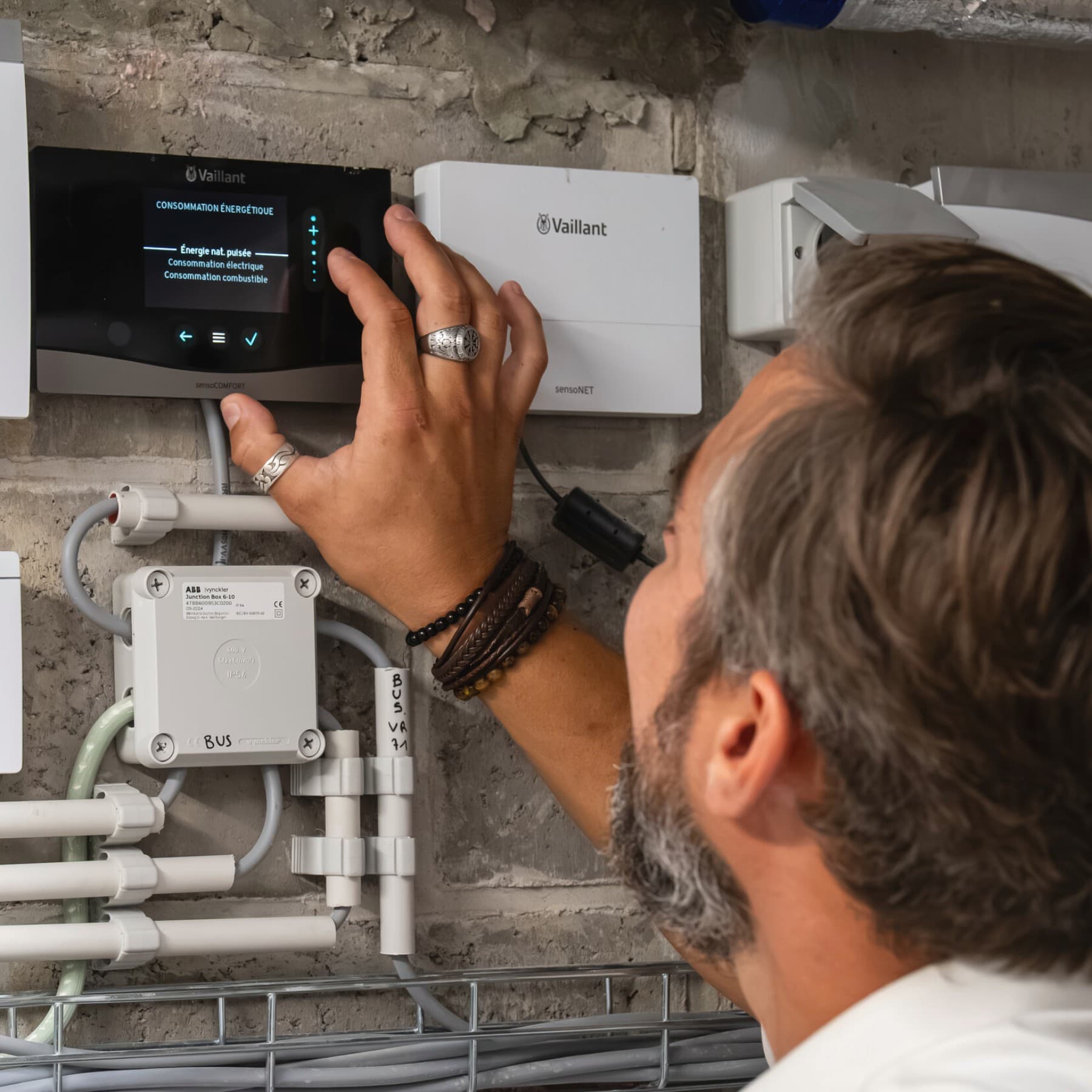 Un homme règle les paramètres du thermostat ; à côté de celui-ci se trouve un module Internet