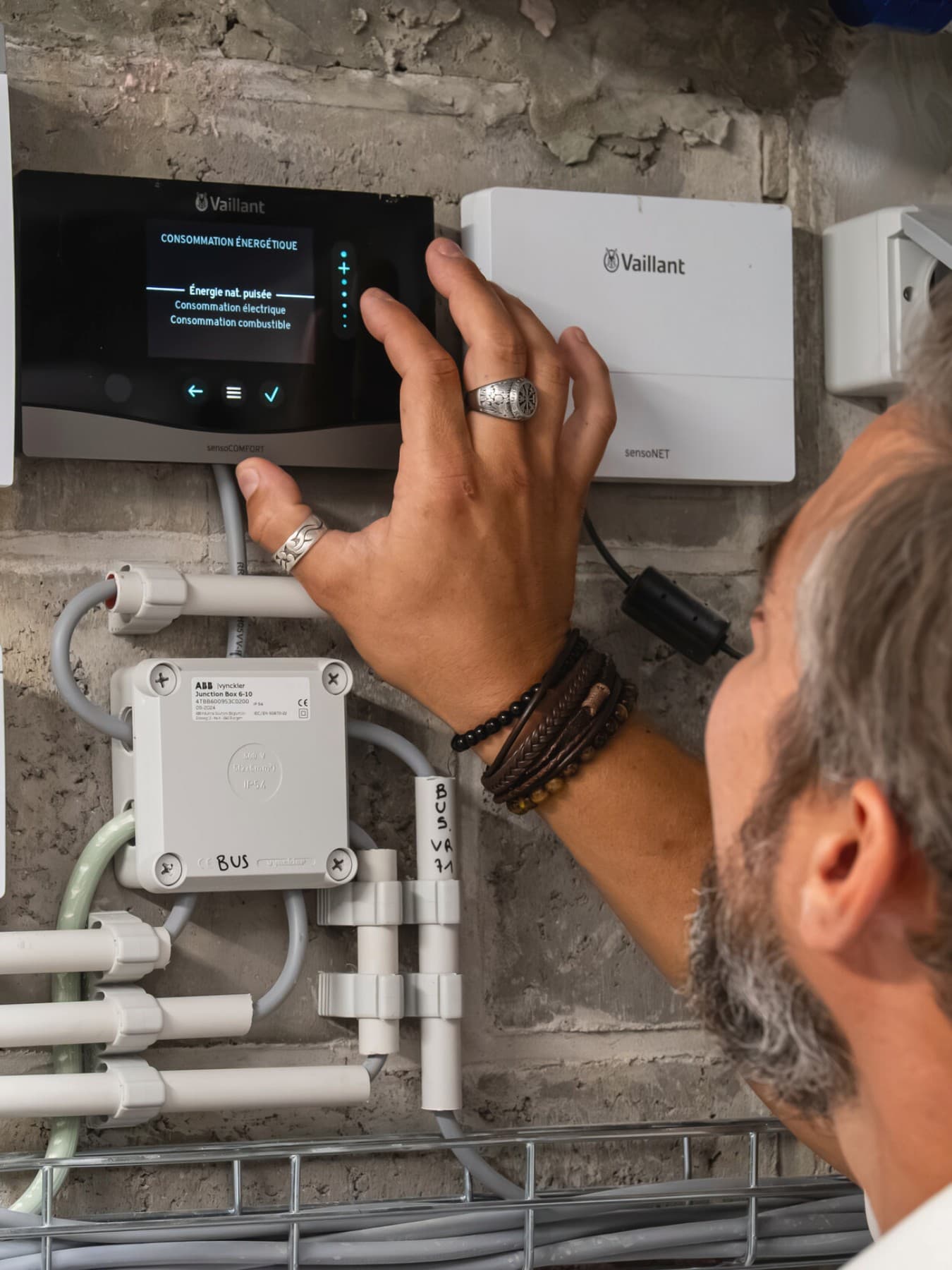 Un homme règle les paramètres du thermostat ; à côté de celui-ci se trouve un module Internet