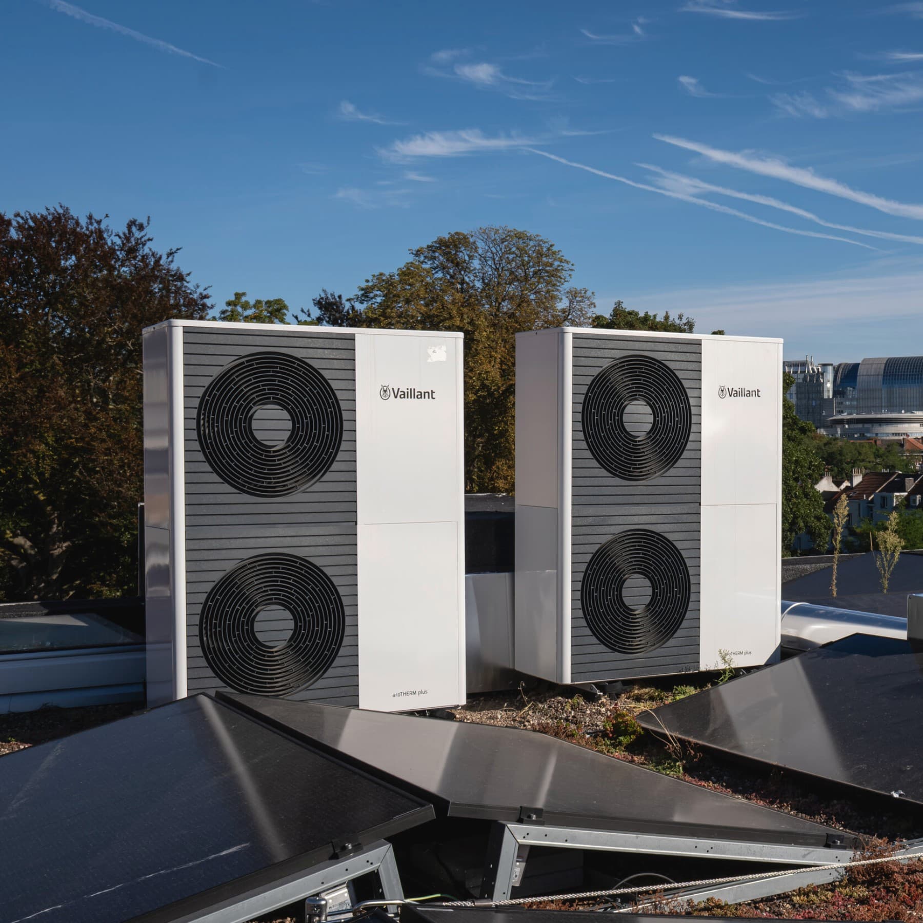 Deux pompes à chaleur doubles sur un toit, avec des panneaux solaires devant les unités extérieures