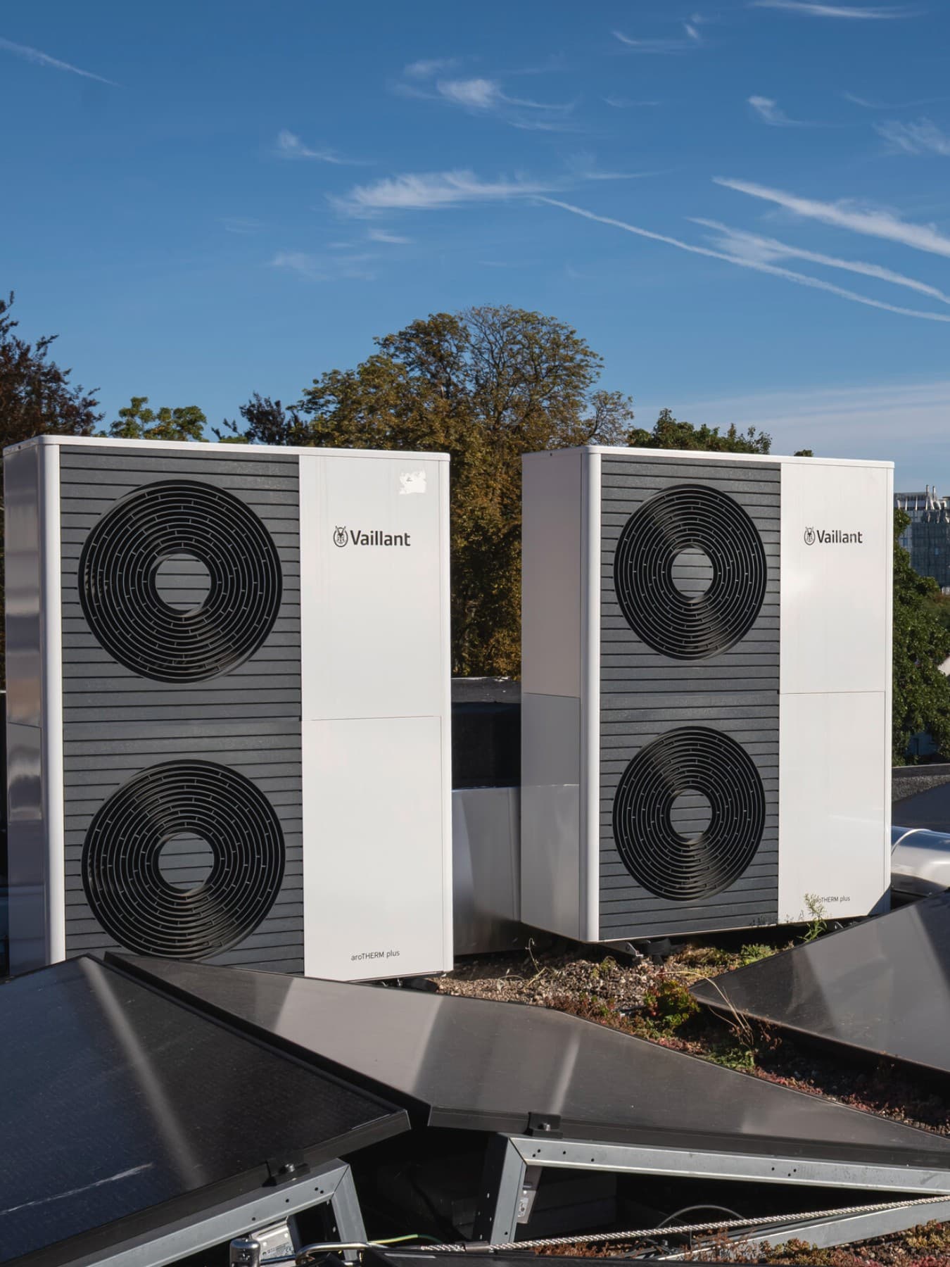 Deux pompes à chaleur doubles sur un toit, avec des panneaux solaires devant les unités extérieures