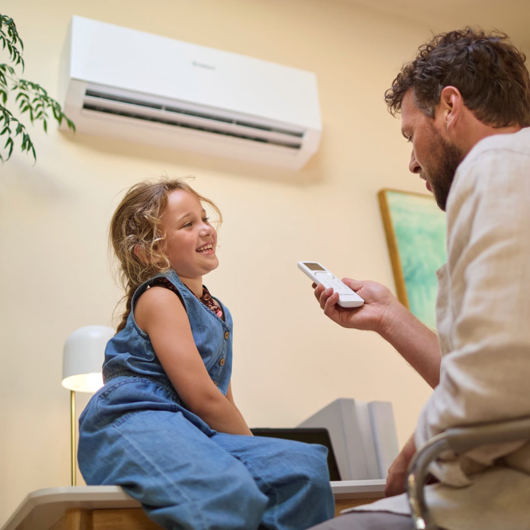 Kind zit op een tafel terwijl een man de airco instelt met een afstandsbediening
