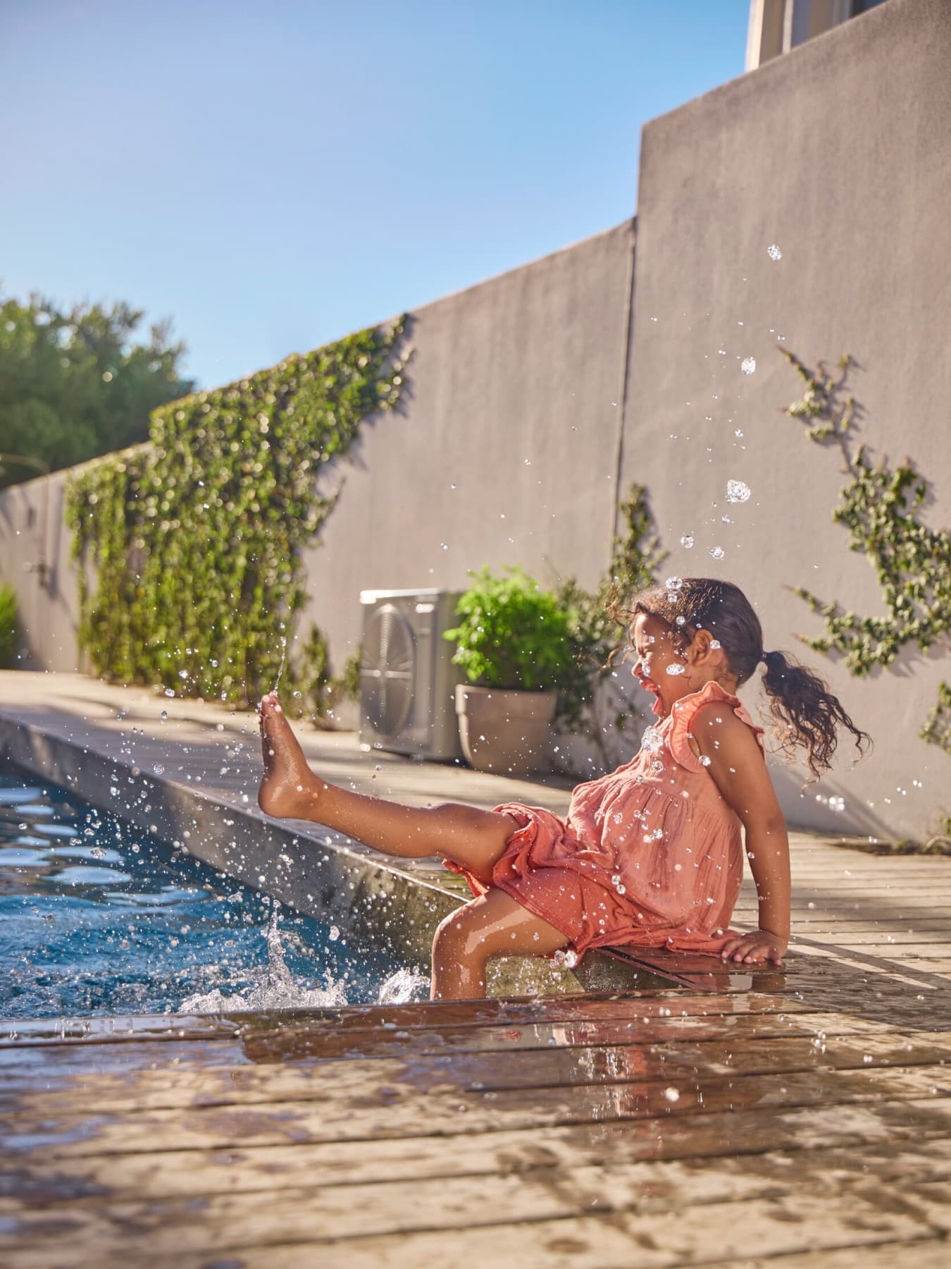 Un enfant est assis sur le rebord d'une plate-forme en bois au bord d'une piscine et joue avec l'eau
