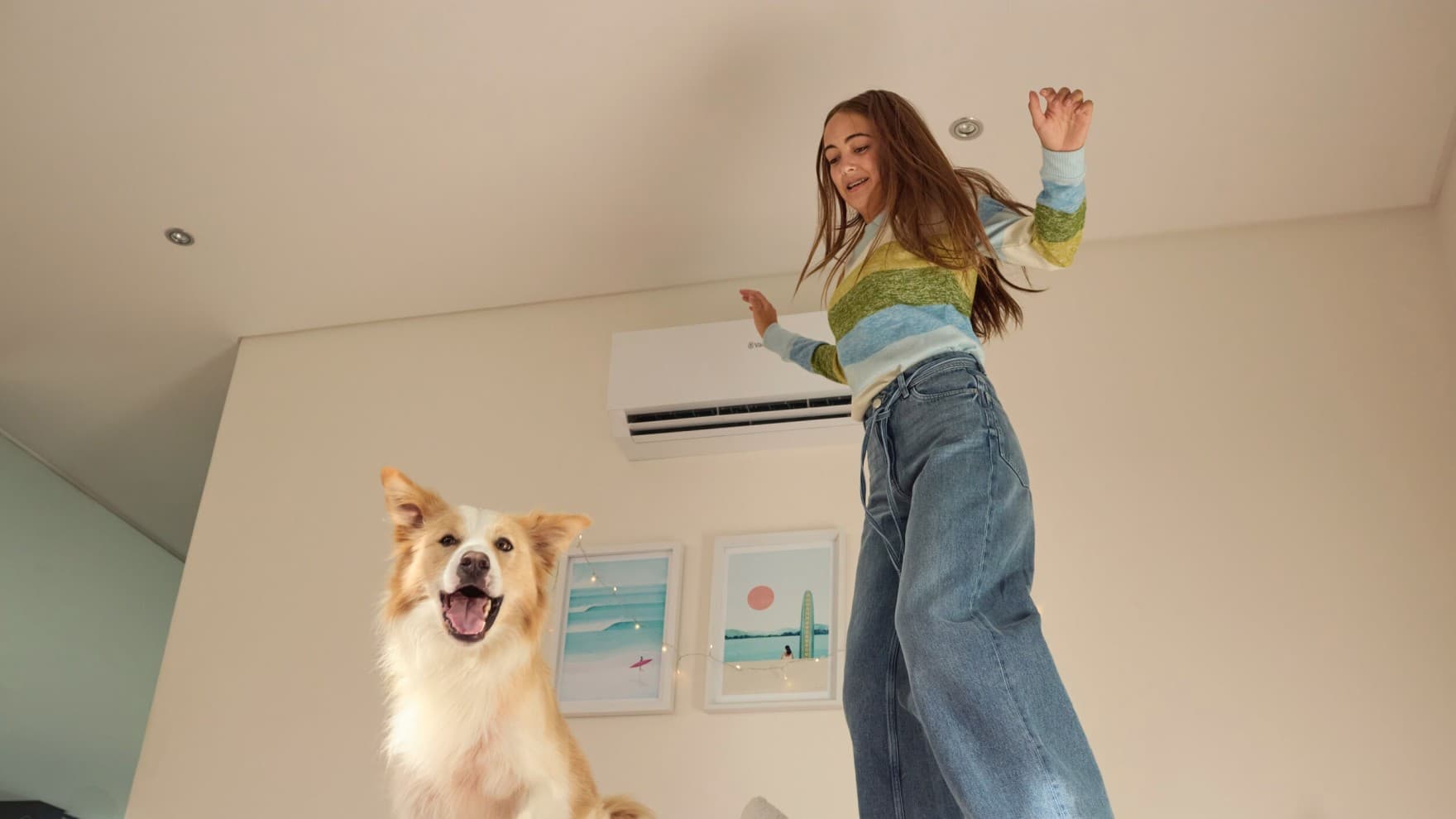 Une fillette saute sur le lit avec son chien ; à l'arrière-plan, on aperçoit l'unité intérieure d'un climatiseur