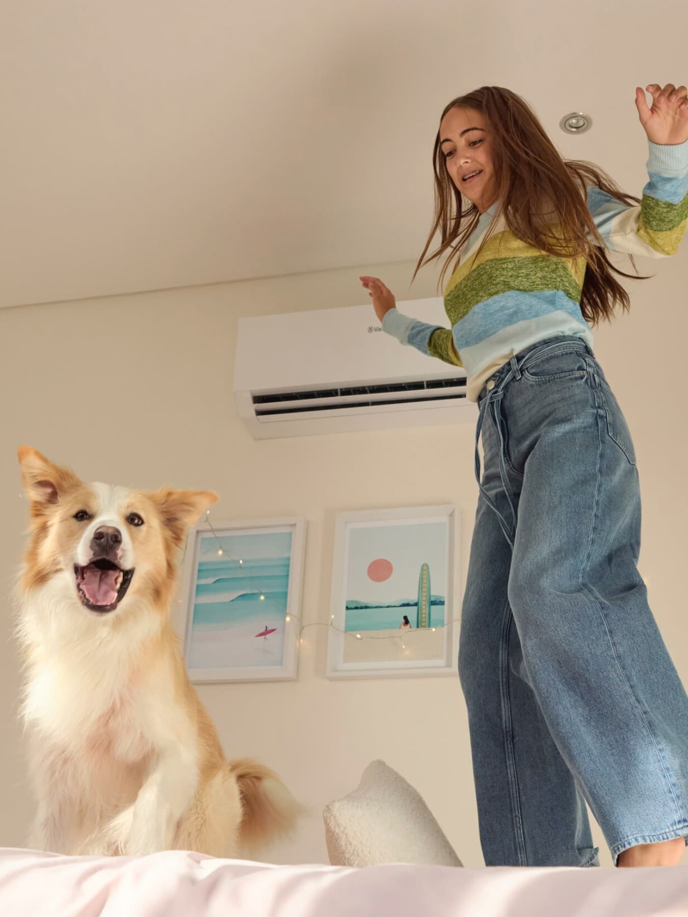 Une fillette saute sur le lit avec son chien ; à l'arrière-plan, on aperçoit l'unité intérieure d'un climatiseur