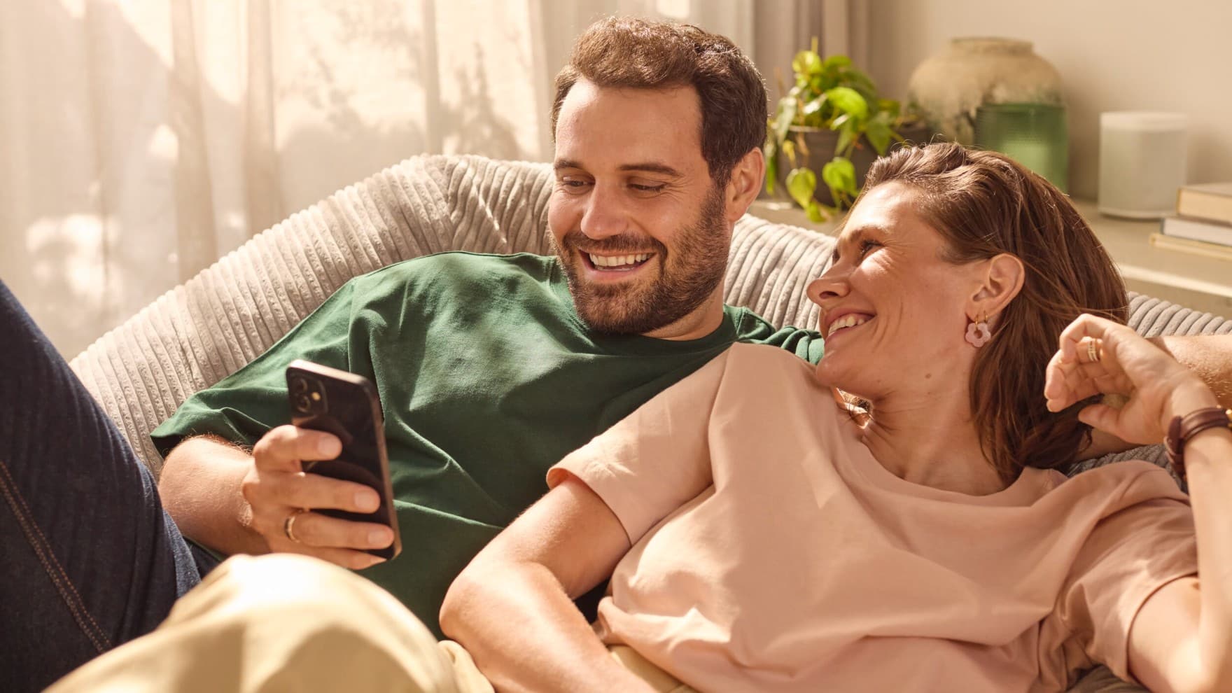 Man en vrouw liggen in zetel en kijken samen naar een smartphone