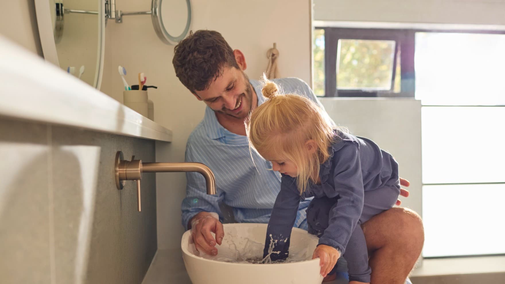 Un père et sa fille jouant avec de l'eau dans un évier