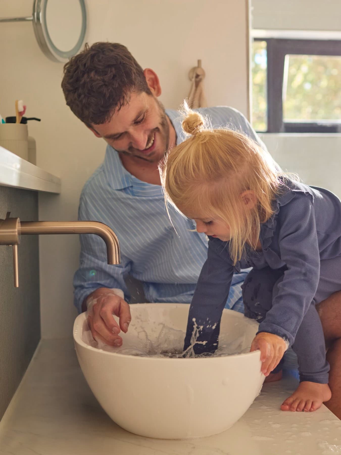 Un père et sa fille jouant avec de l'eau dans un évier