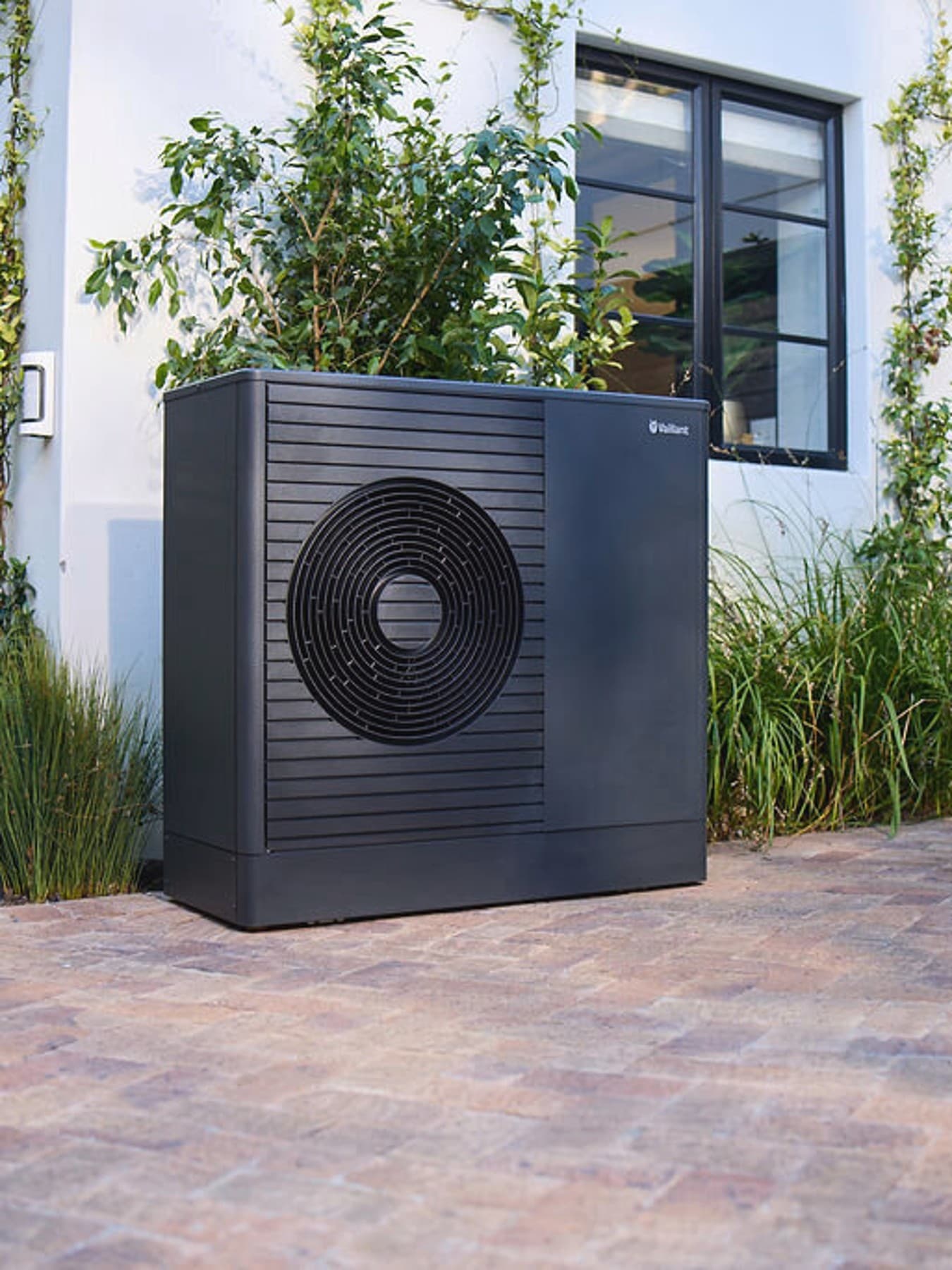 Pompe à chaleur Dark Vaillant aroTHERM plus dans le jardin devant une maison