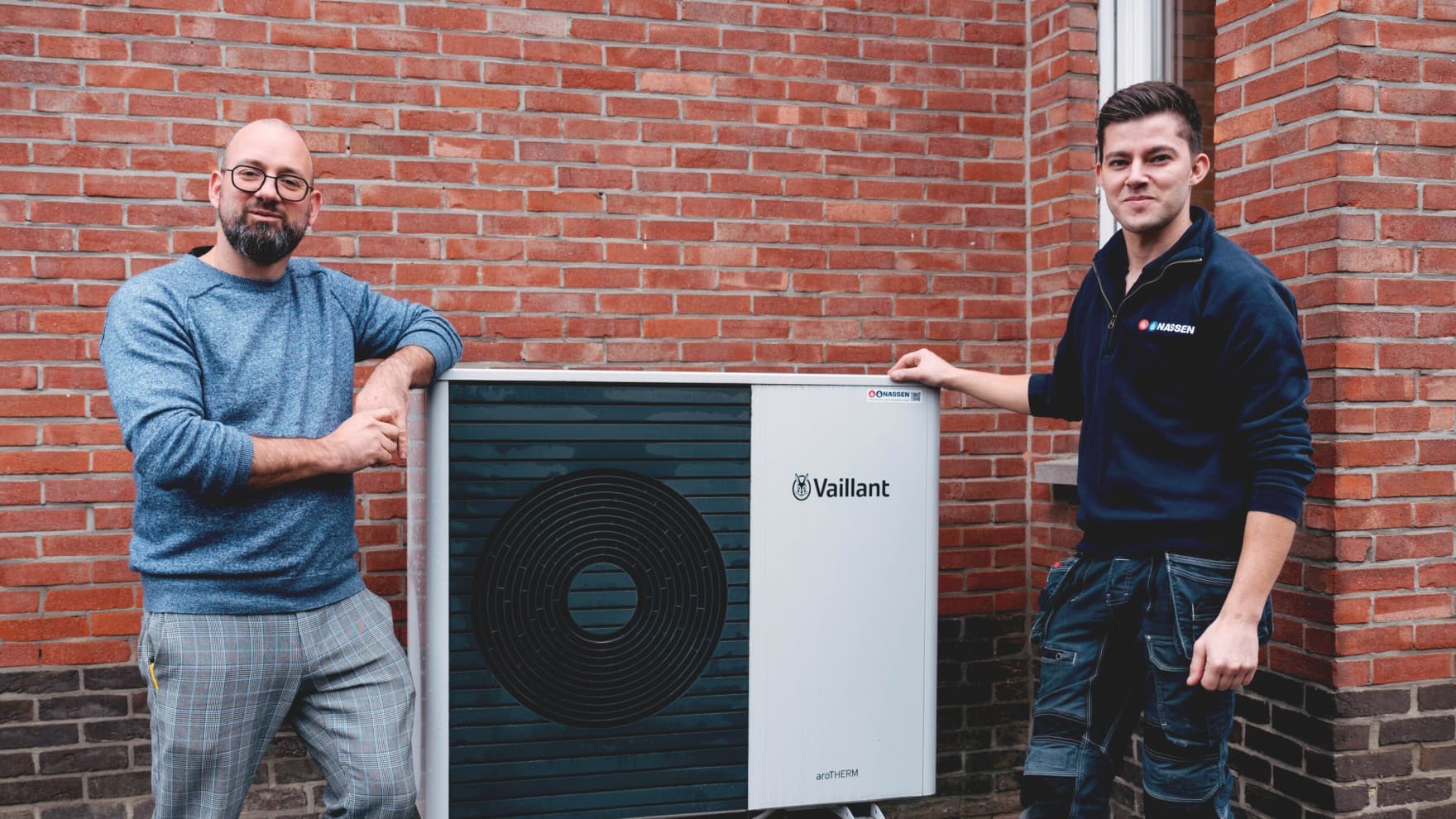 The customer and the installer are standing next to the outdoor unit of a heat pump