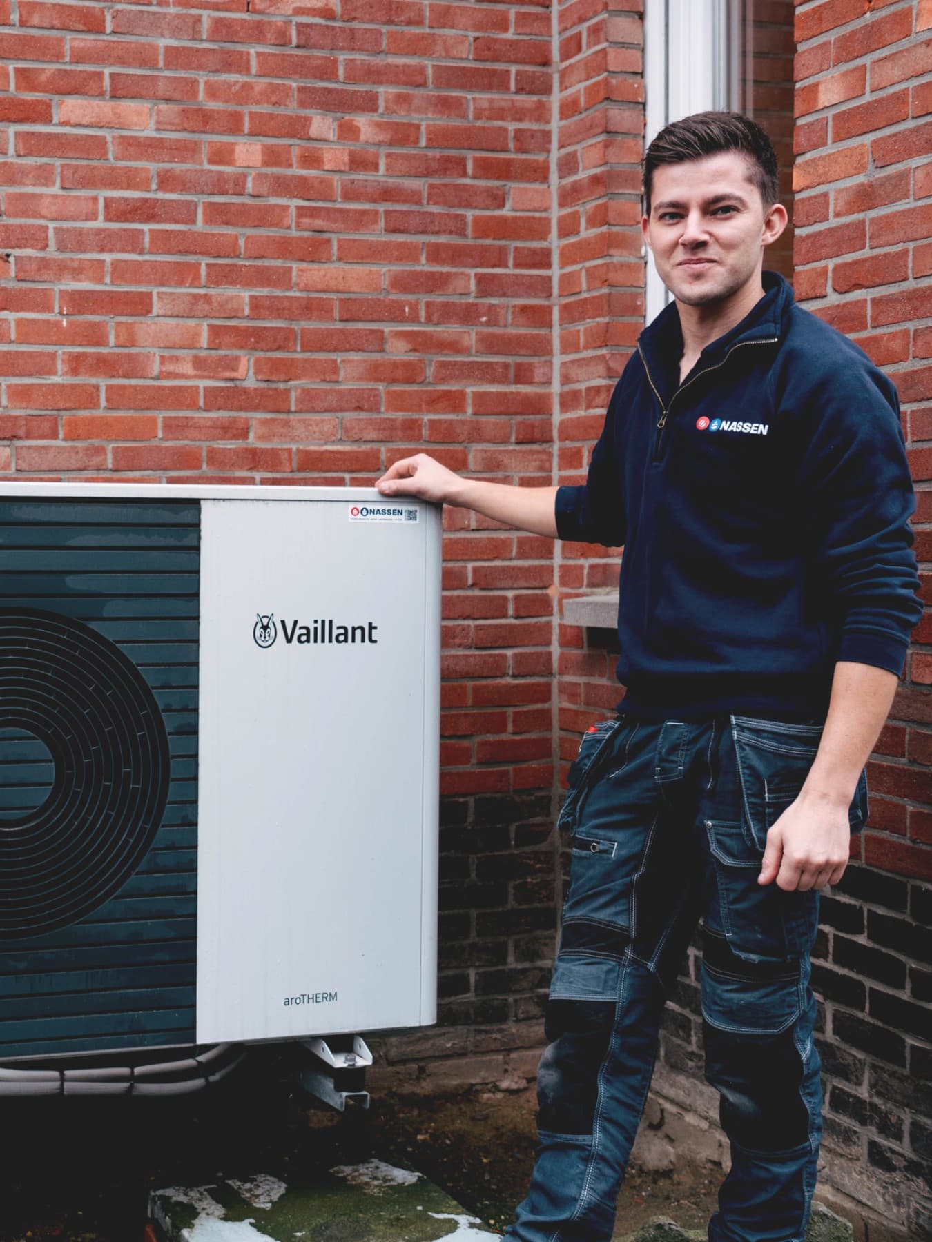 The customer and the installer are standing next to the outdoor unit of a heat pump