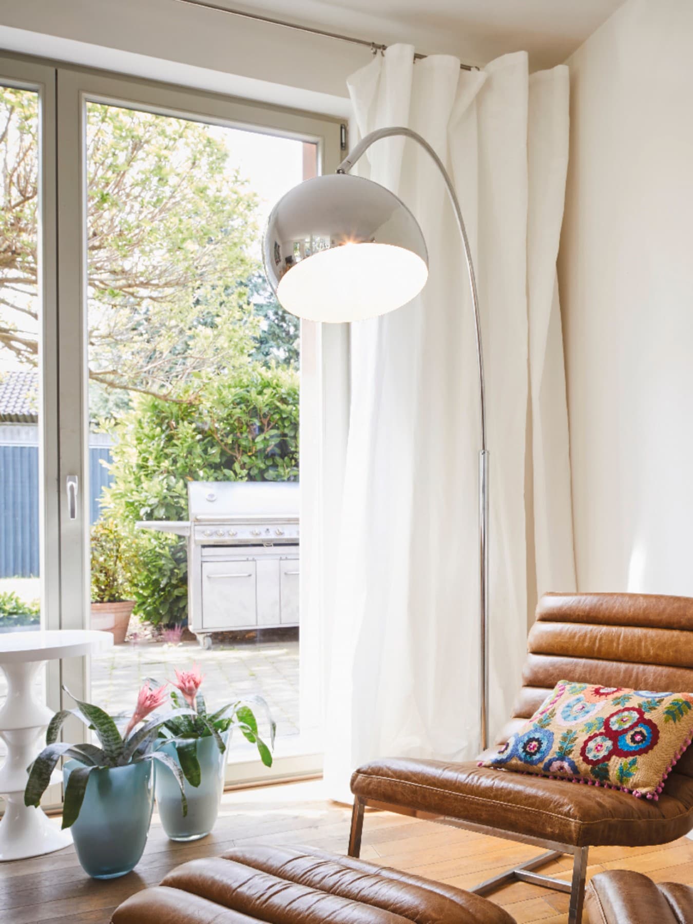Des fauteuils en cuir marron avec des coussins aux couleurs vives, à côté d'une lampe ronde argentée