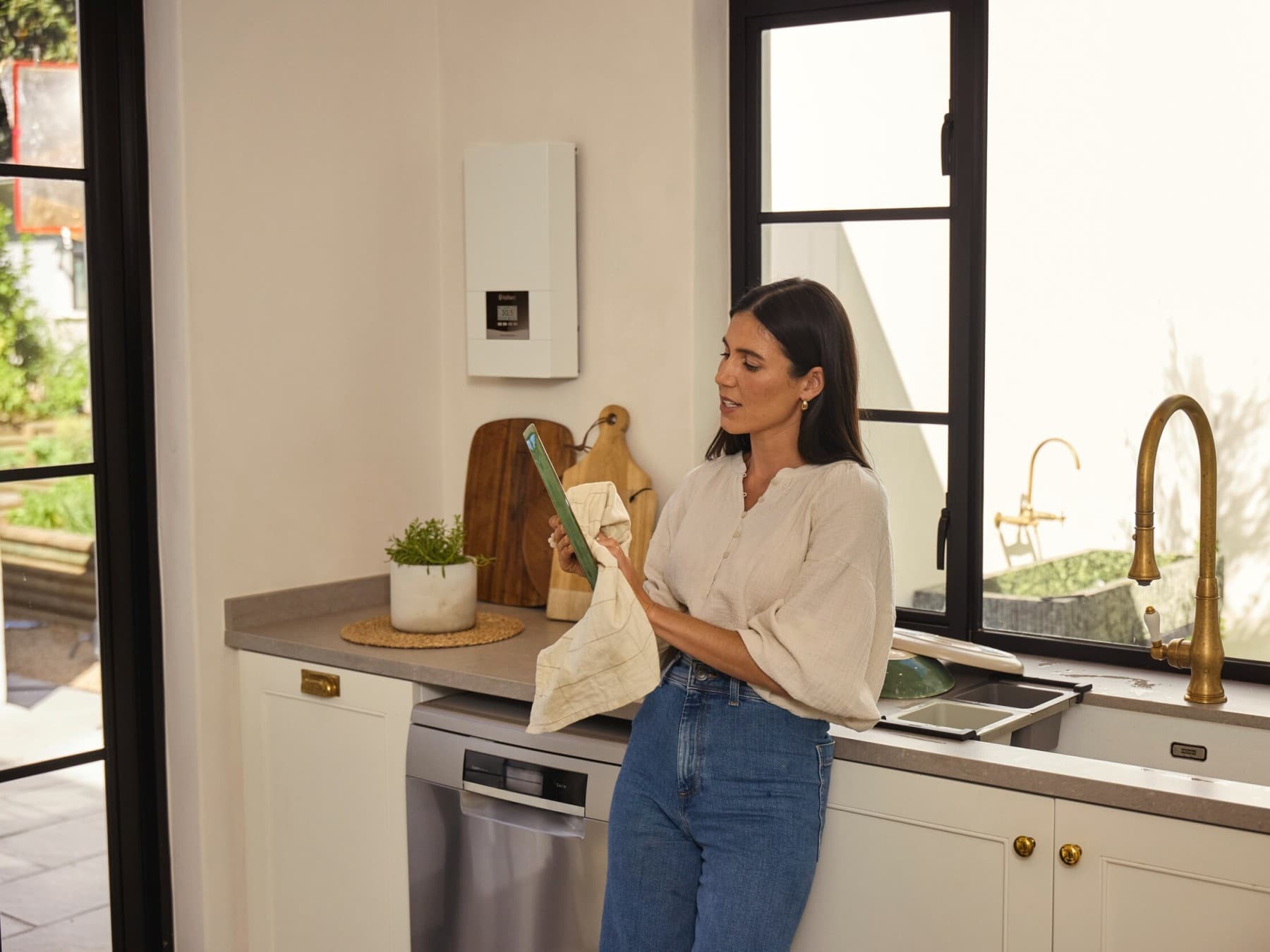 Une femme fait la vaisselle dans la cuisine. À l'arrière-plan, on aperçoit le chauffe-eau électrique electronicVED accroché au mur.
