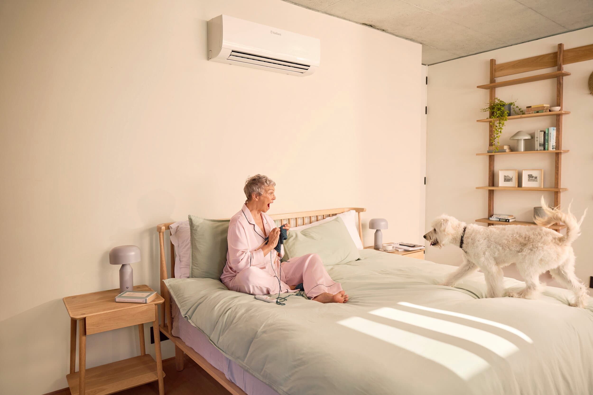 Une femme est assise dans son lit tandis que son chien s'approche d'elle