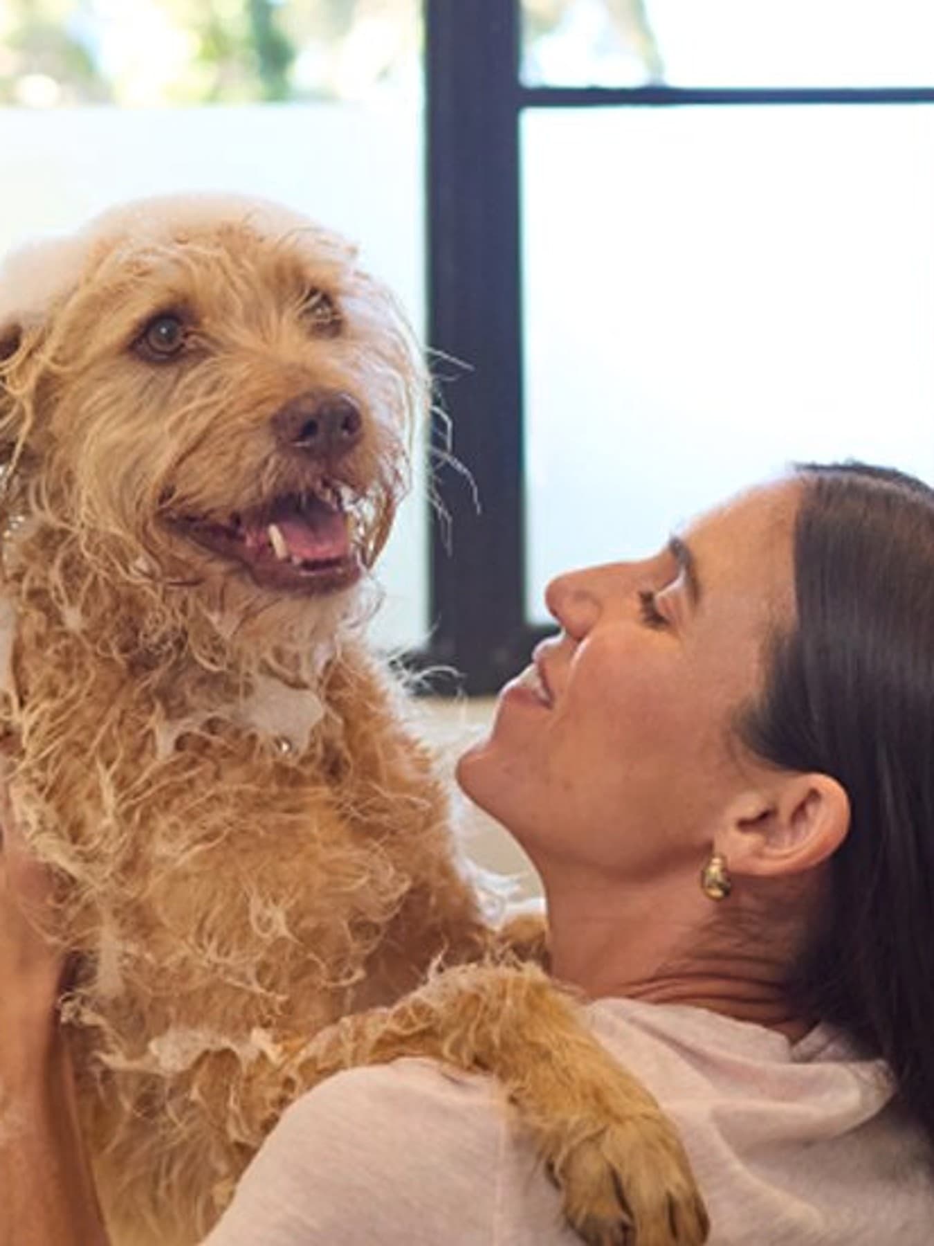Une femme lave un chien beige dans une baignoire, le chien halète