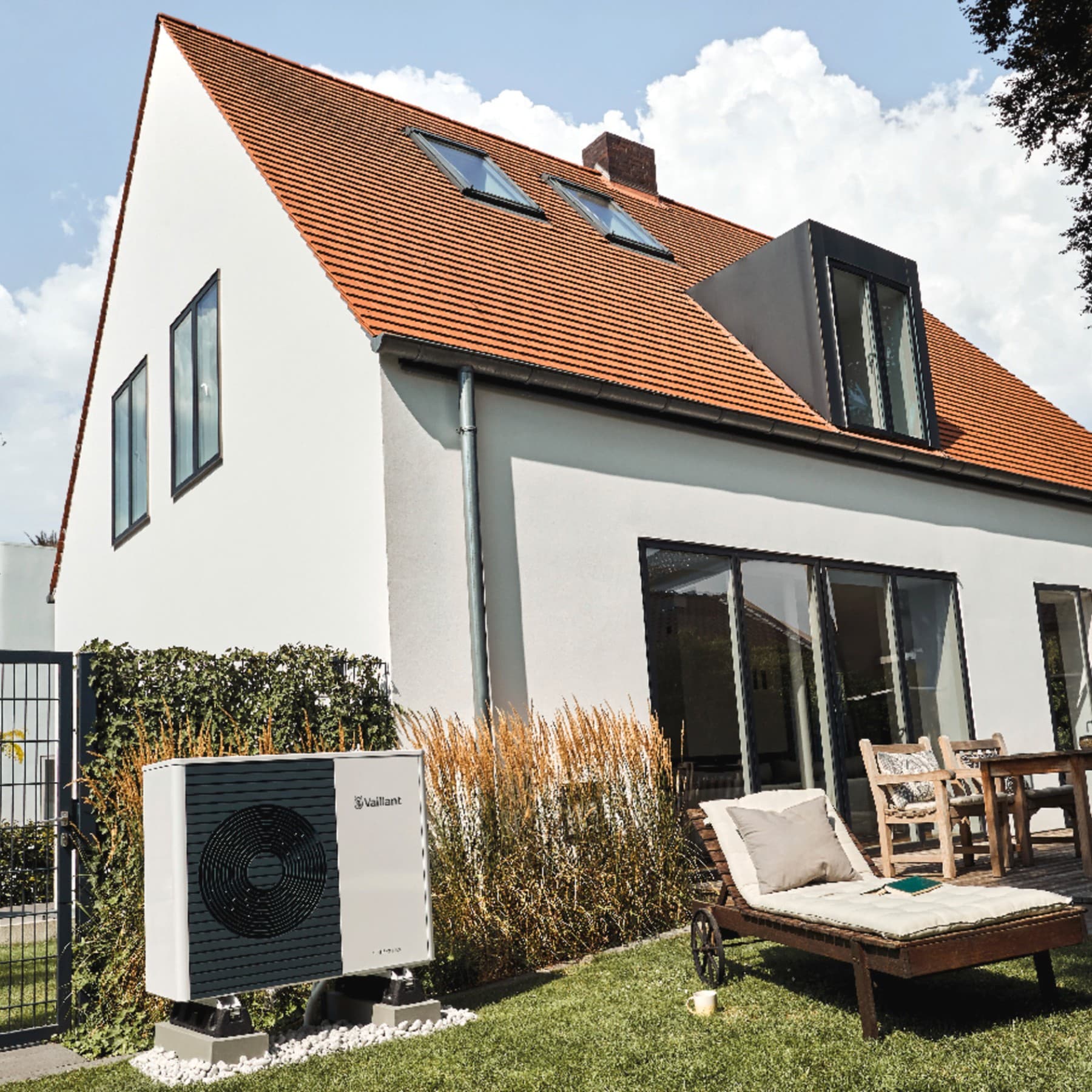 Maison en crépi blanc avec des encadrements de fenêtres noirs. Des chaises longues sont disposées dans le jardin.