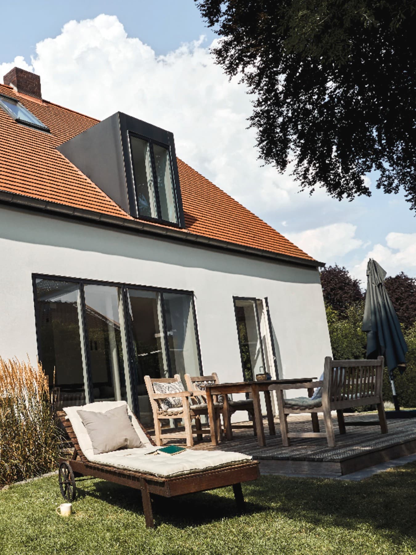Maison en crépi blanc avec des encadrements de fenêtres noirs. Des chaises longues sont disposées dans le jardin.
