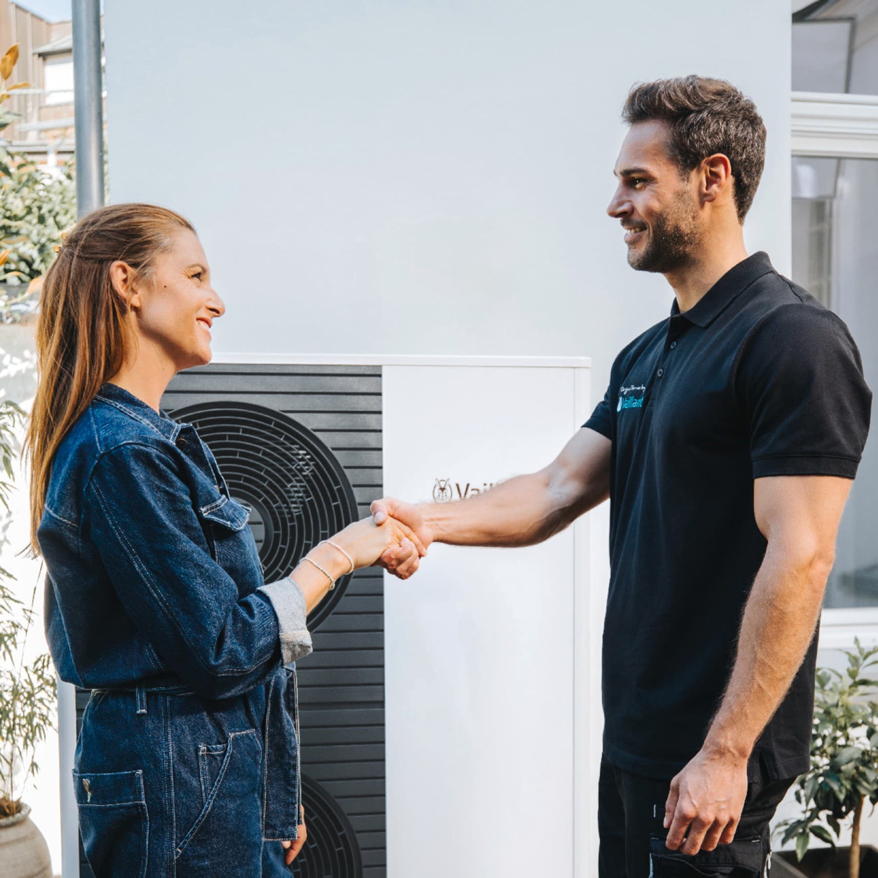 Une femme et un technicien Vaillant se serrent la main devant une pompe à chaleur.