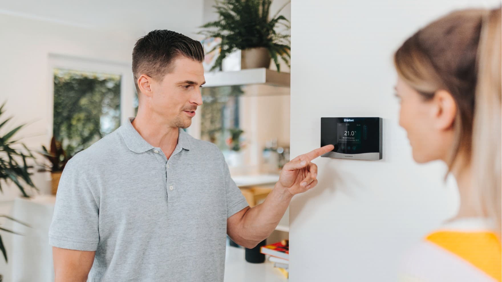 Un installateur donne des explications sur un thermostat tandis qu'une femme l'écoute