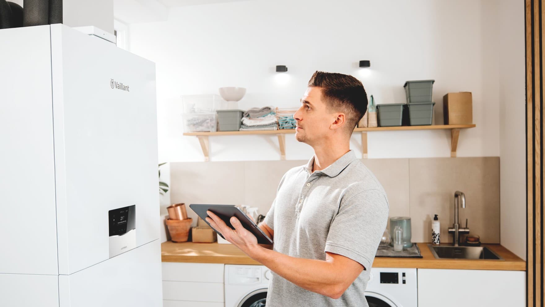 Installateur staat voor een geothermische warmtepomp van Vaillant met een tablet in zijn handen.