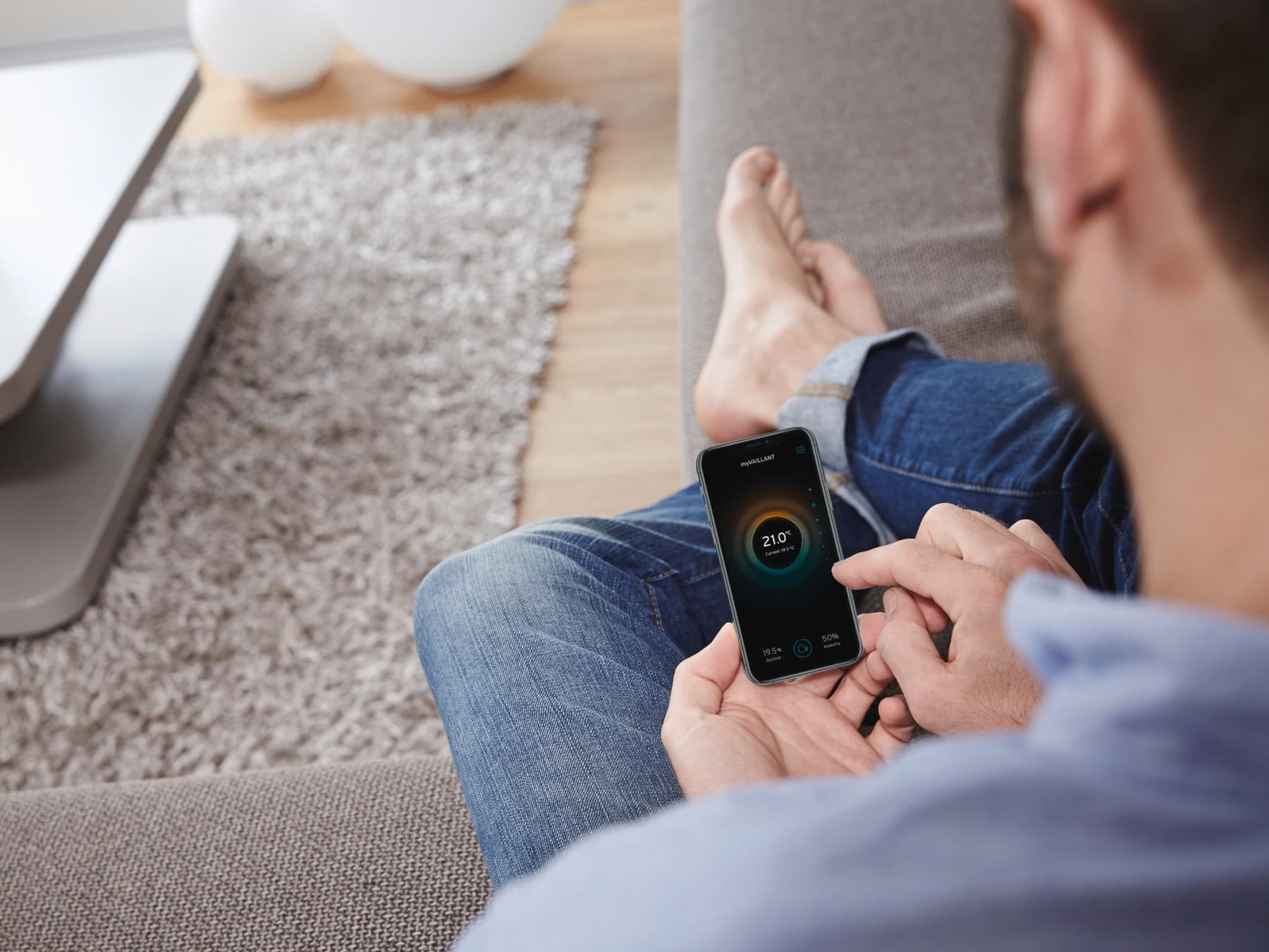 Un homme est assis dans son canapé et utilise son application myVaillant