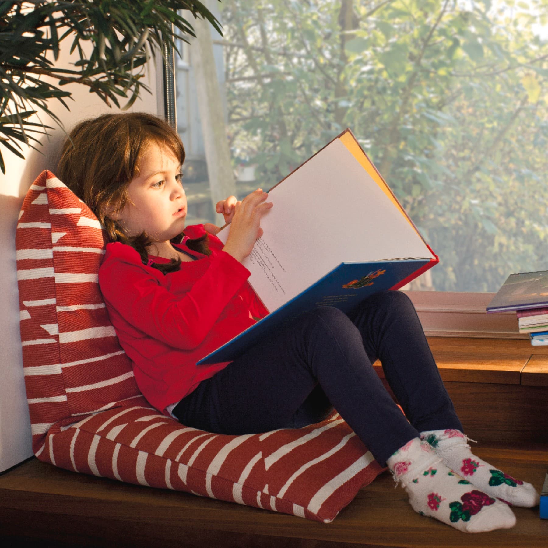Un enfant lit un livre près de la fenêtre.