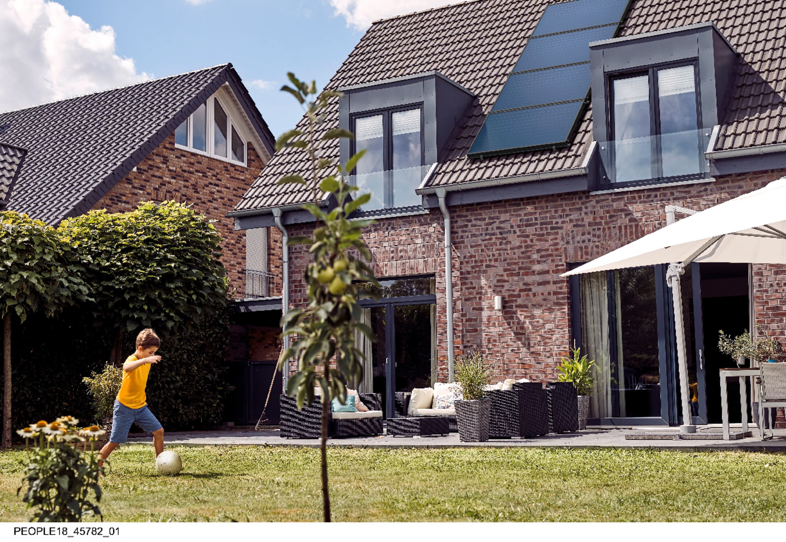 Un garçon joue dans le jardin ; à l'arrière-plan, on aperçoit un toit équipé de panneaux solaires