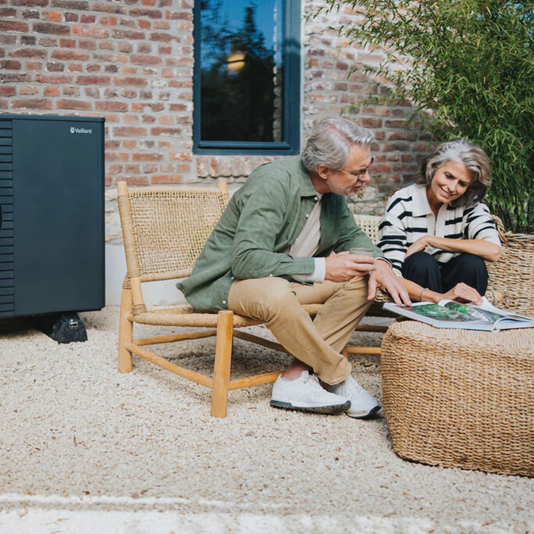 Een stel zit buiten in de tuin en bekijkt een brochure. Op de achtergrond staat een Vaillant-warmtepomp.
