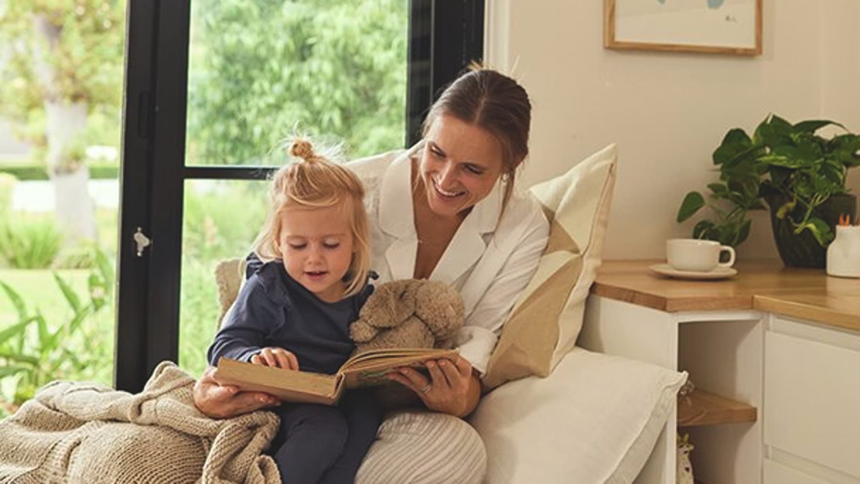 La mère est assise sur un canapé et lit un livre à une petite fille.