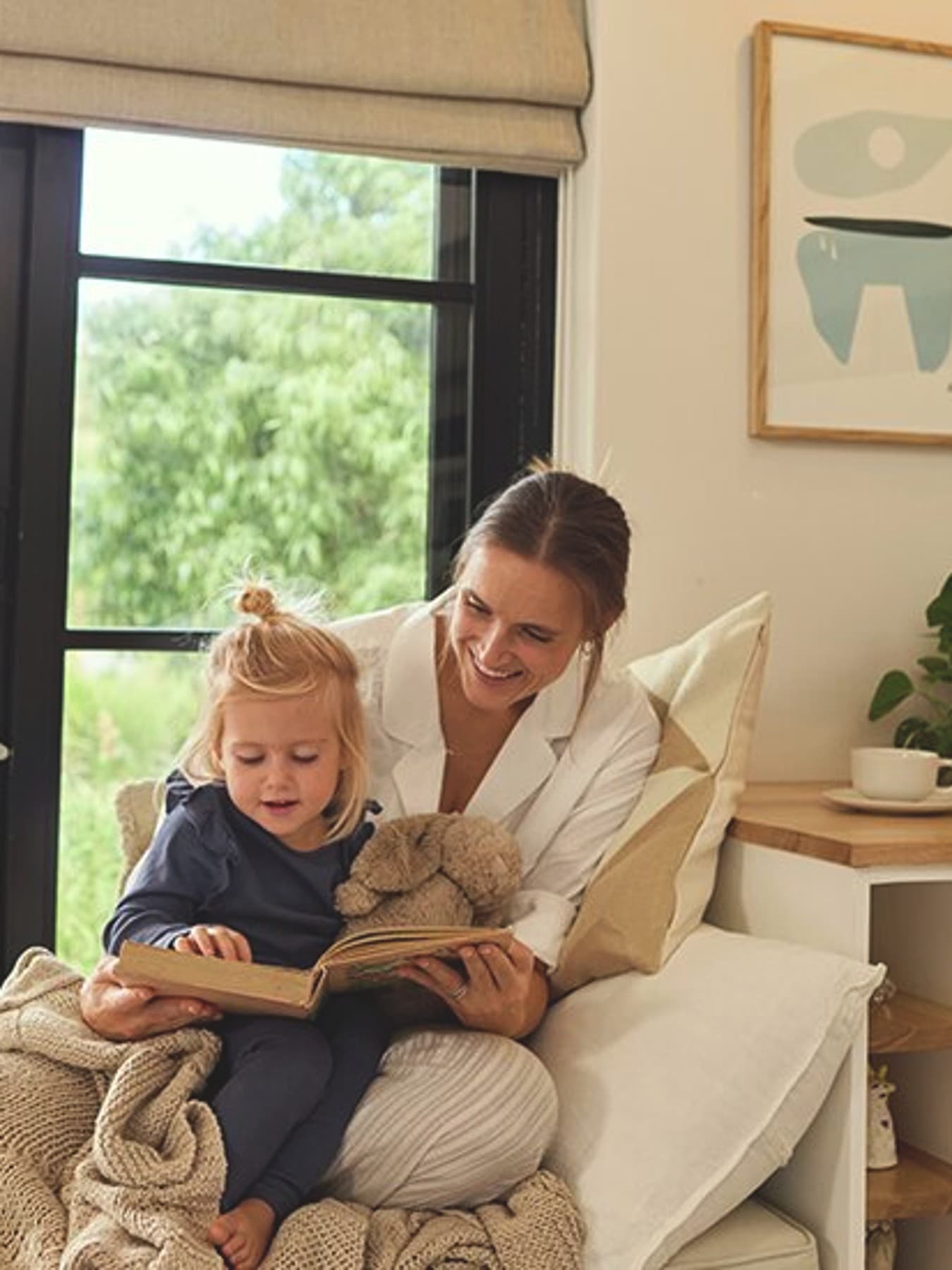 La mère est assise sur un canapé et lit un livre à une petite fille.