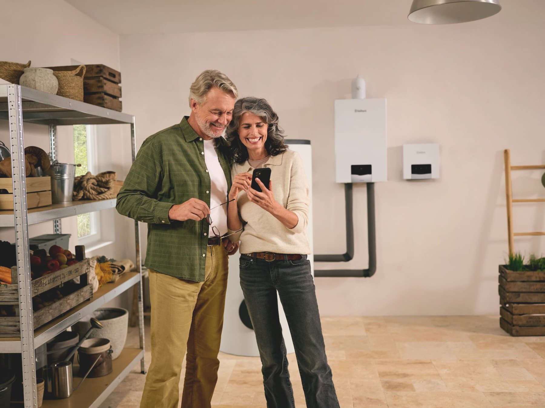 Un couple regarde un téléphone dans un local de rangement, avec des produits Vaillant en arrière-plan.