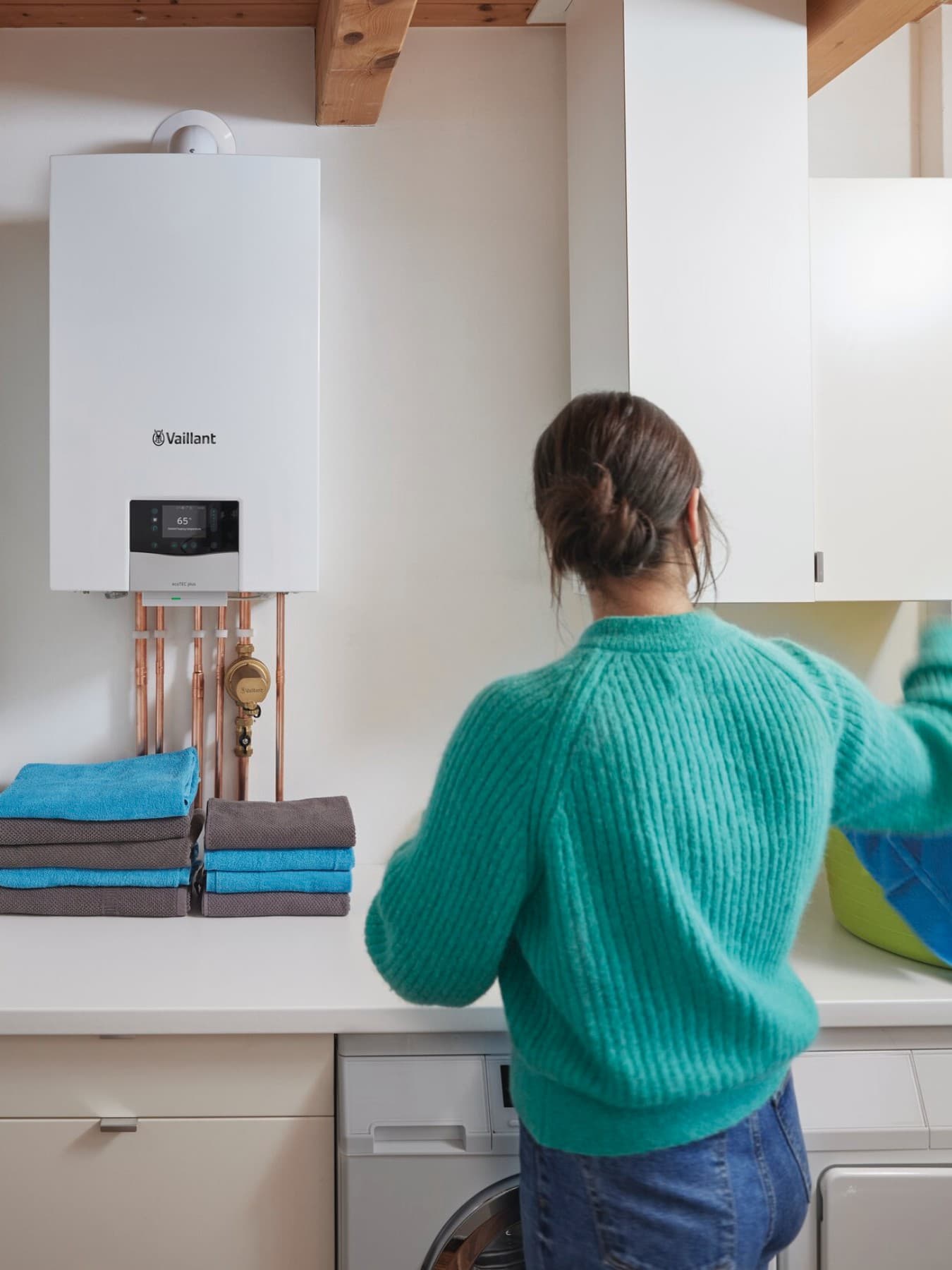 Une femme fait sa lessive, avec une chaudière et un chauffe-eau mural Vaillant en arrière-plan.