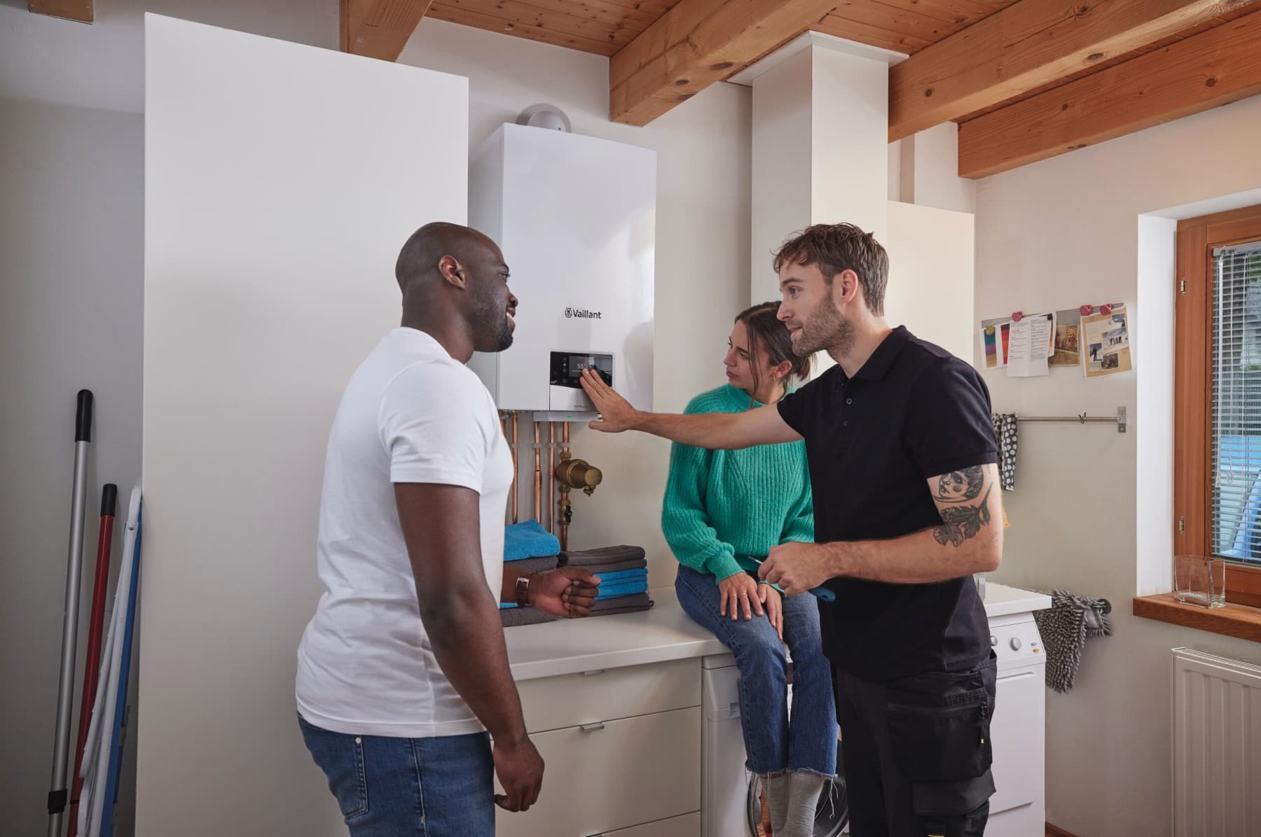 Un technicien donne quelques explications à un couple à côté d'une chaudière murale Vaillant